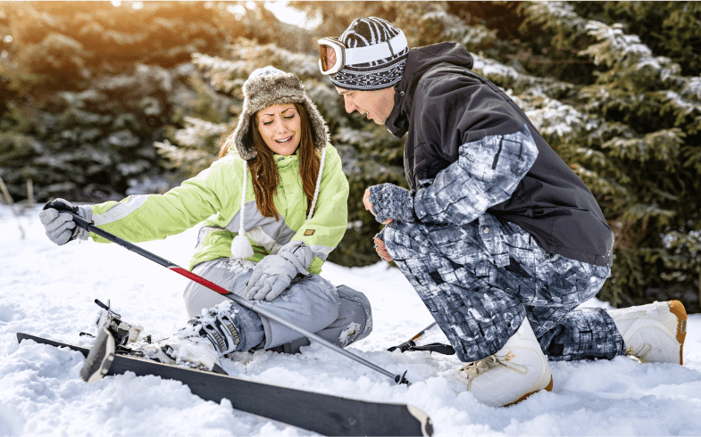 Mężczyzna pomaga kontuzjowanej kobiecie na stoku narciarskim